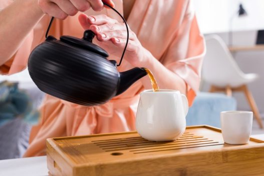 Kvinde der hælder te op i en kop fra en tekande